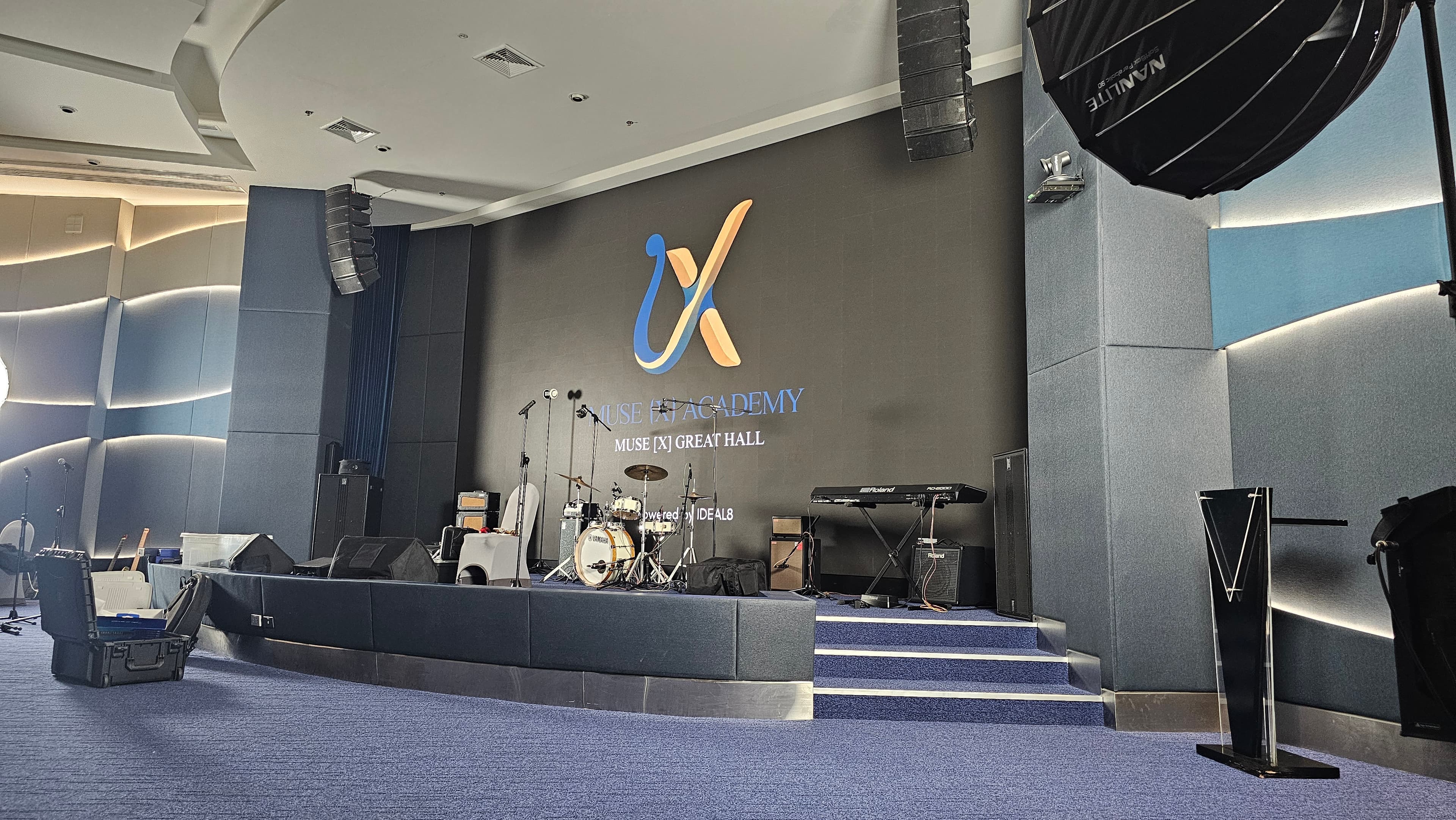 Stage-facing setup inside The Great Hall with the Muse [X] Academy mark visible on the back wall.